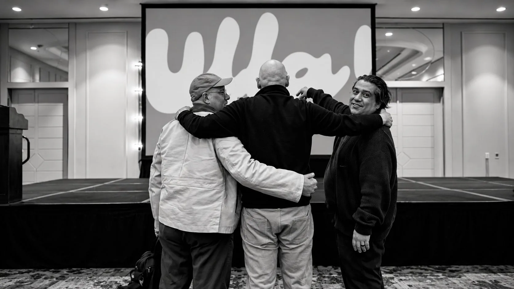 Manuel Kairé, Willy Paiz y Wicho López, socios de Peter Jordan, abrazados frente a la pantalla de UFFA!